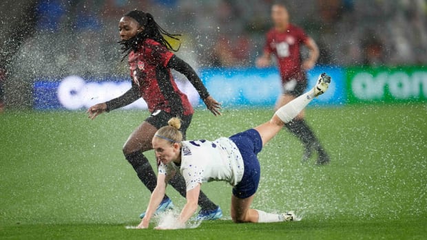 A USWNT player falls to the ground as water splashes up from the grass